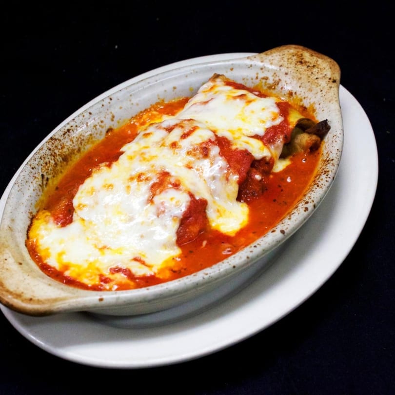 Baked lasagna with melted mozzarella cheese and red sauce in an oval dish on a white plate.