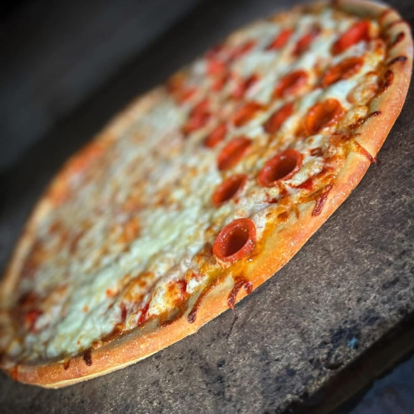A half-pepperoni, half-cheese pizza from Genova's Italian Restaurant on a dark surface.