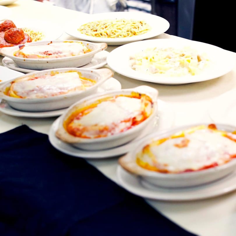 Multiple Italian dishes, including baked pasta, spaghetti with meatballs, and fettuccine alfredo, on a white table.