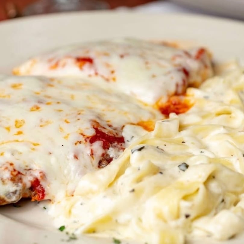 Chicken parmesan with melted cheese and red sauce, served alongside creamy fettuccine alfredo.